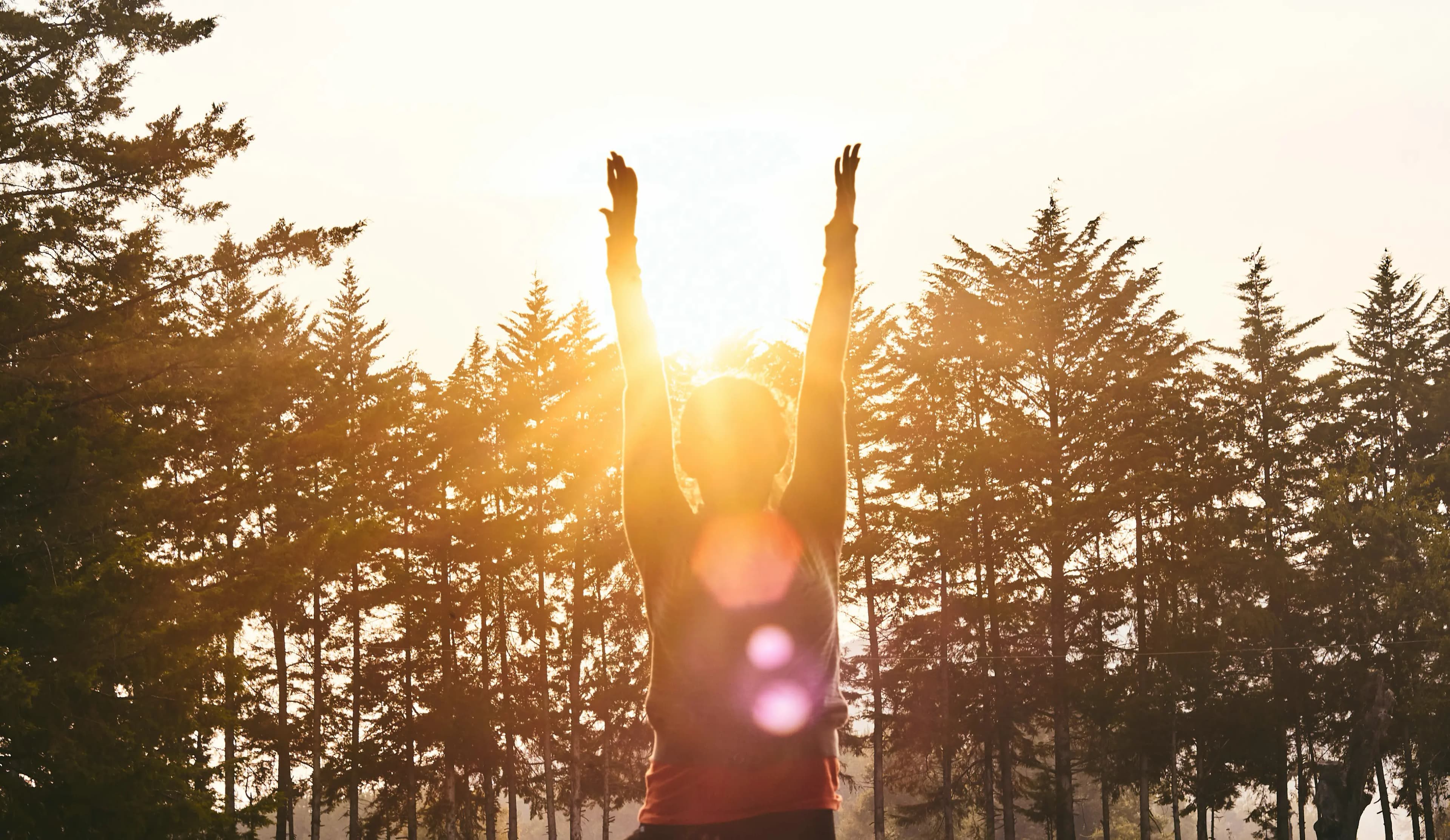 Rose Long sat leading a retreat class in cross-legged position on the floor, smiling with her eyes closed. She is sat in-front of a large bay window which looks out onto a large sun-filled garden. There is a large, golden gong to her left and a plant with a himilayan salt lamp on her right.